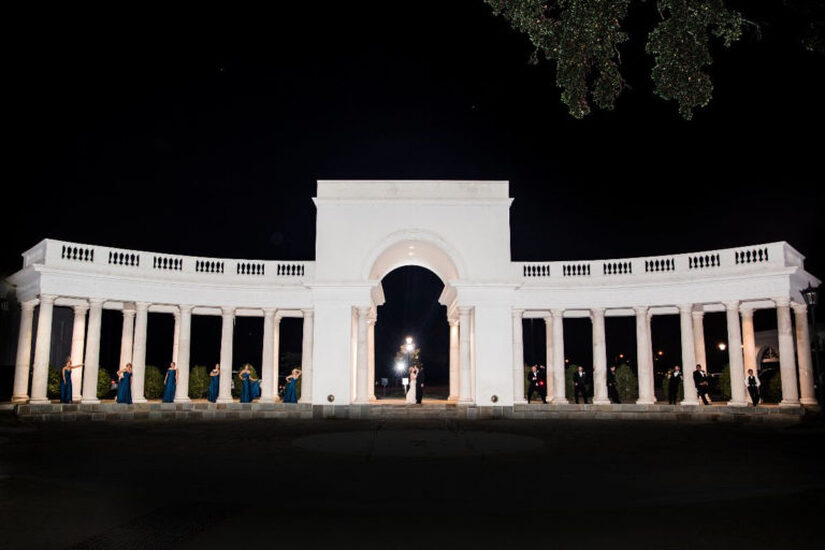 Image of the Colonnade at night with bride and  groom under the arches and bridesmaids and men under the columns - outdoor wedding venues - lafayette la - Le Pavillon